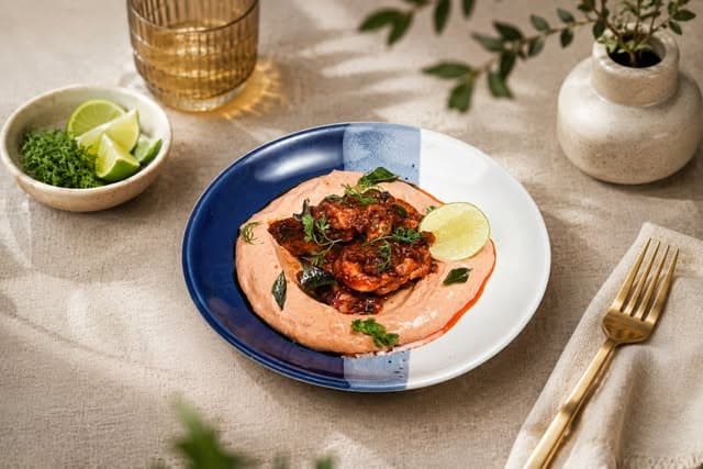 Spiced prawns served over labneh with curry leaves and lime, on a blue and white ceramic plate