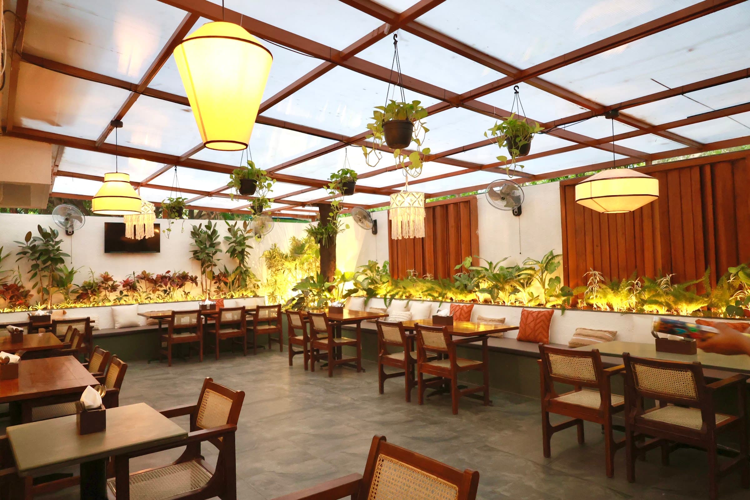 The garden room at Ouza — timber pergola, hanging lanterns, cane chairs and dense planting