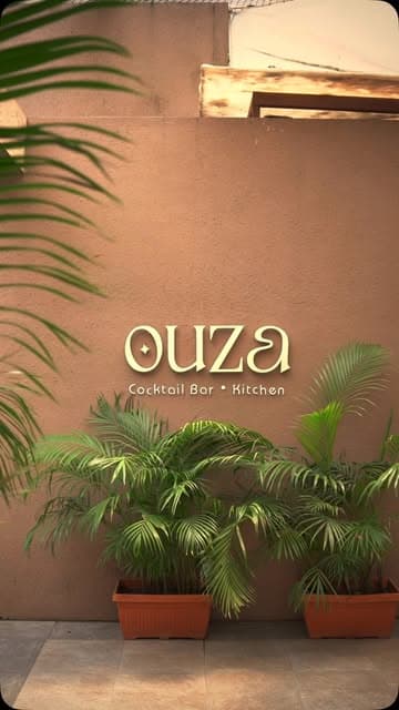 The OUZA sign on a terracotta wall, framed by palms